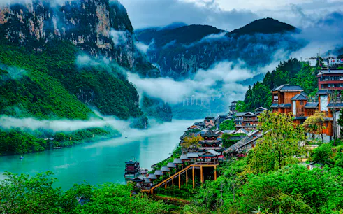 Chongqing river view with traditional wooden buildings and misty mountains.