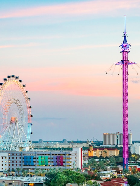 Ferris wheel and tall swing ride at sunset in an urban setting.