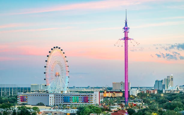 Ferris wheel and tall swing ride at sunset in an urban setting.