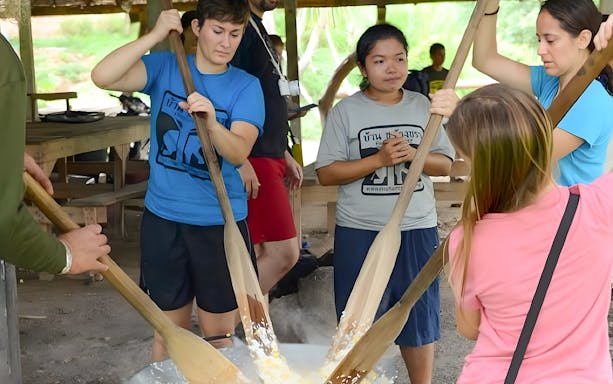 Visitors stirring a large pot at ElephantsWorld Kanchanaburi, engaging in a hands-on activity.