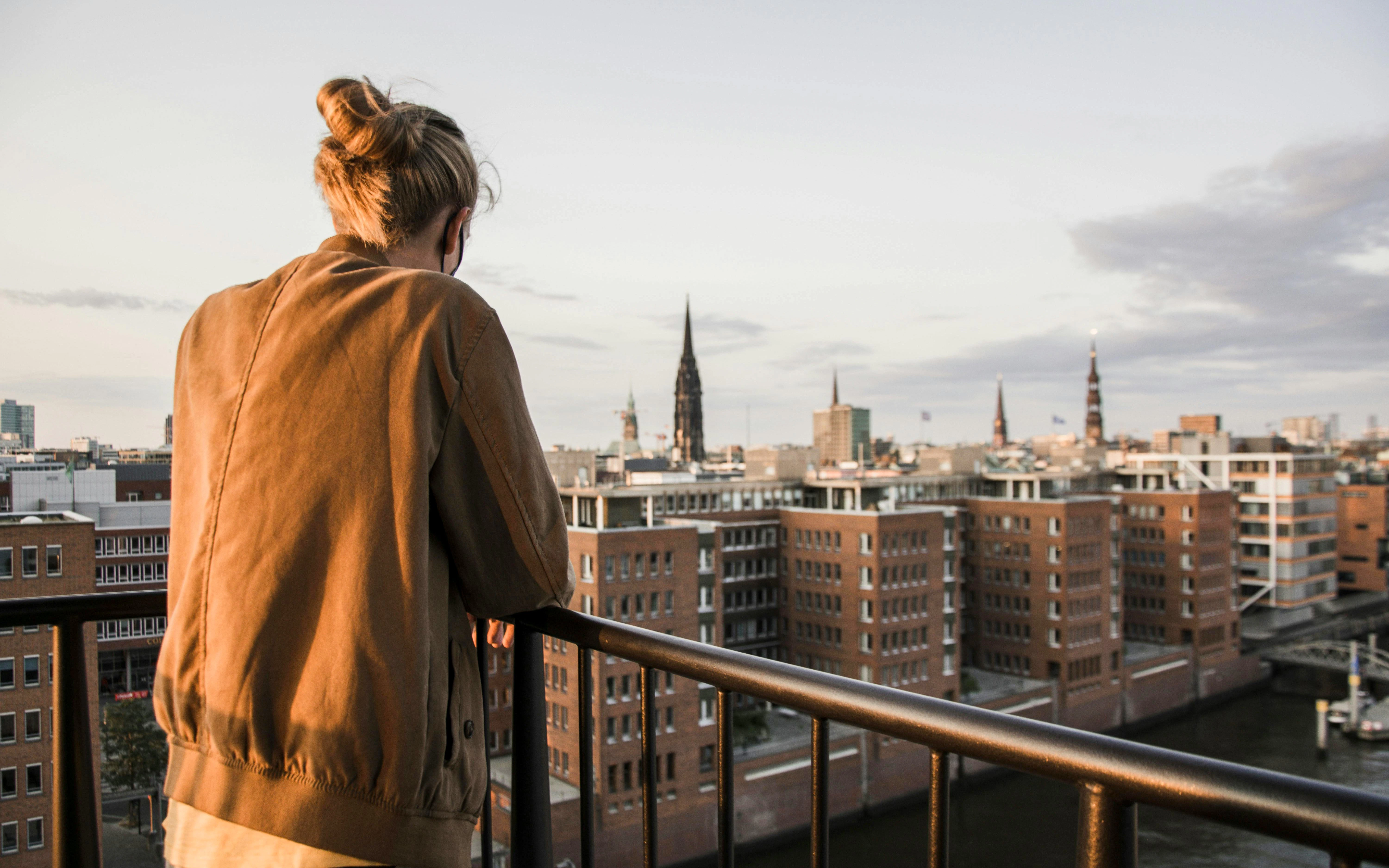 Woman observing Hamburg cityscape from Elbphilharmonie Plaza balustrade.