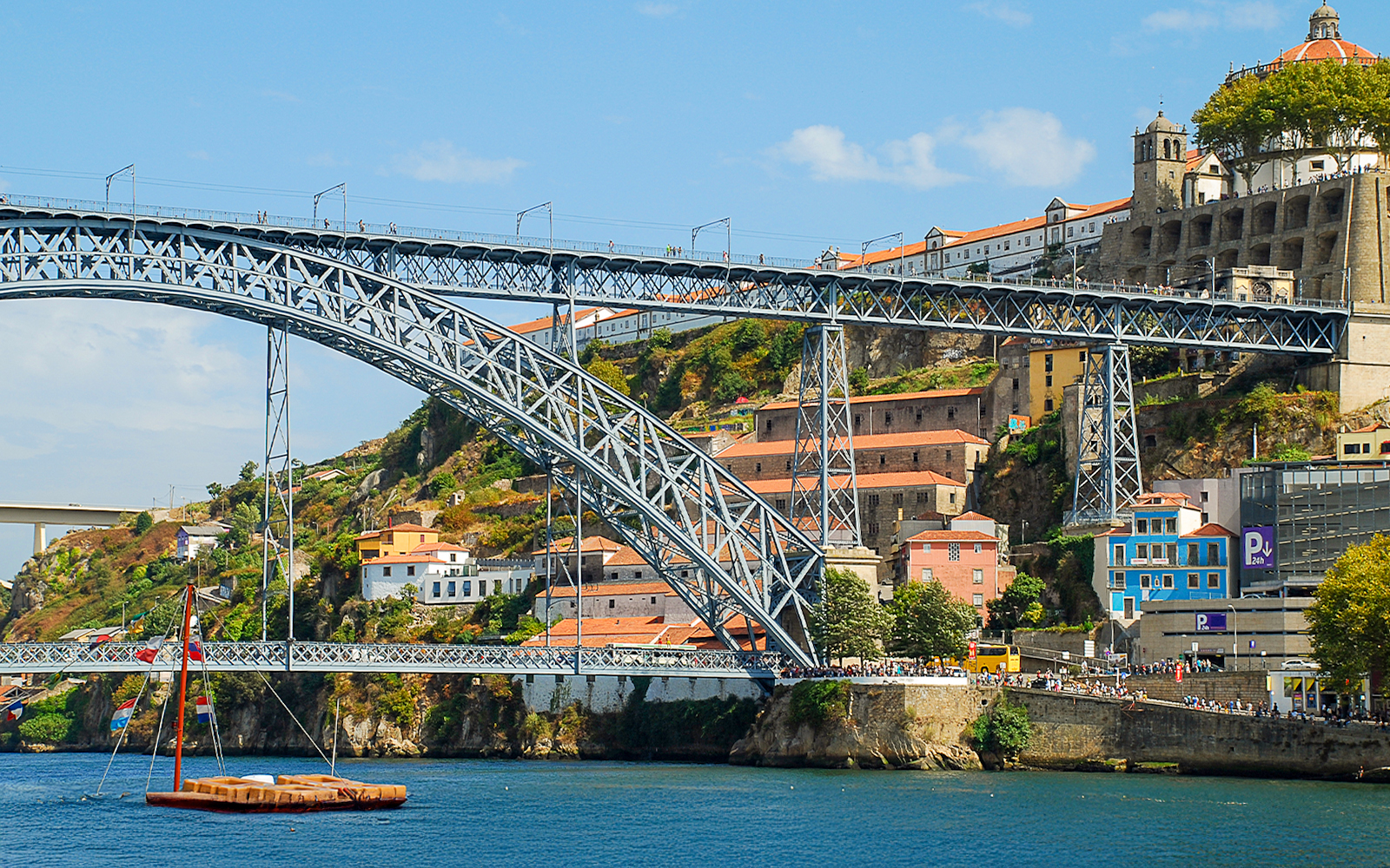 Ponte D. Luís bridge spanning the Douro River in Porto, with colorful buildings and a boat below.