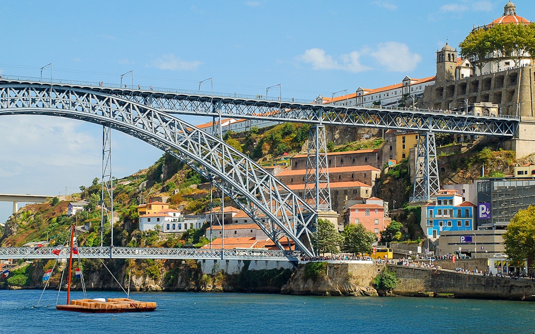 Ponte D. Luís bridge spanning the Douro River in Porto, with colorful buildings and a boat below.