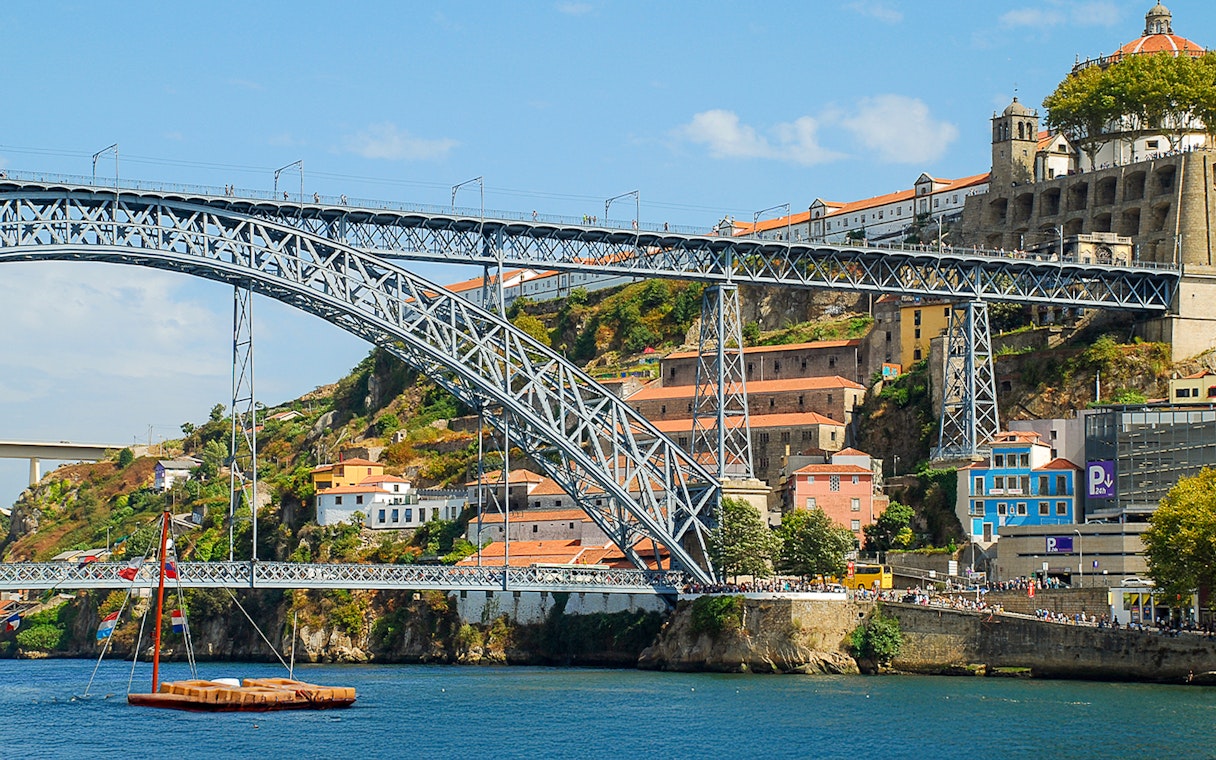 Ponte D. Luís bridge spanning the Douro River in Porto, with colorful buildings and a boat below.