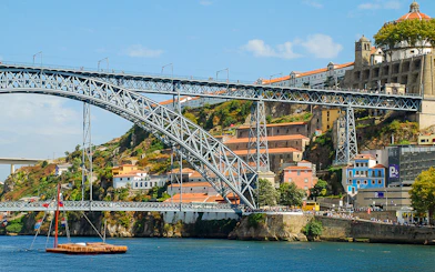 Ponte D. Luís bridge spanning the Douro River in Porto, with colorful buildings and a boat below.