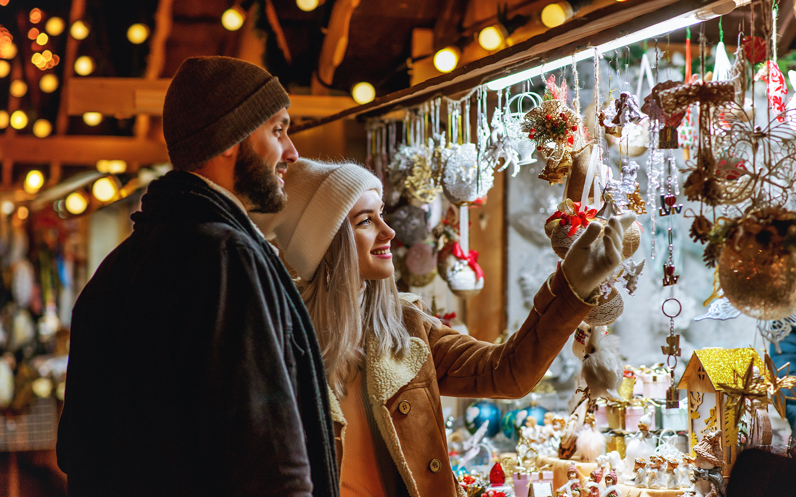 Couple purchasing decorations at a Christmas market in a festive setting.
