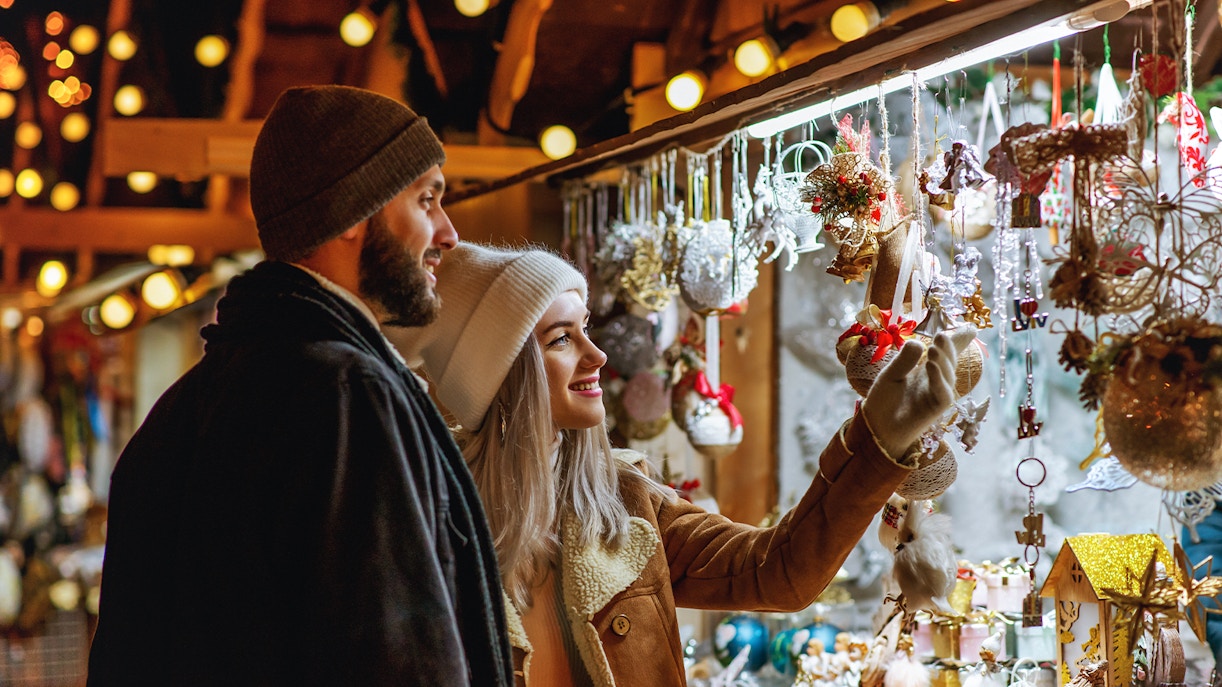 Couple exploring a festive Christmas market stall with ornaments in Europe.