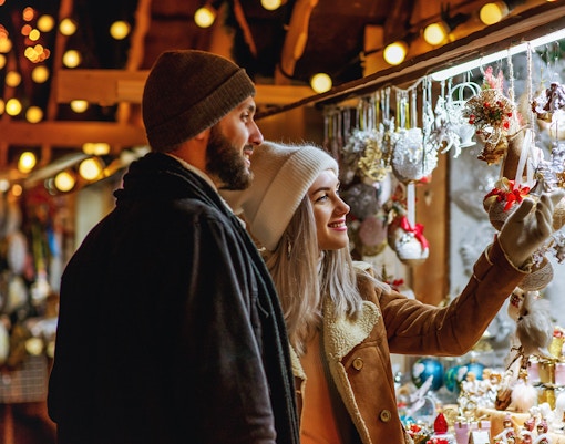 Couple exploring a festive Christmas market stall with ornaments in Europe.