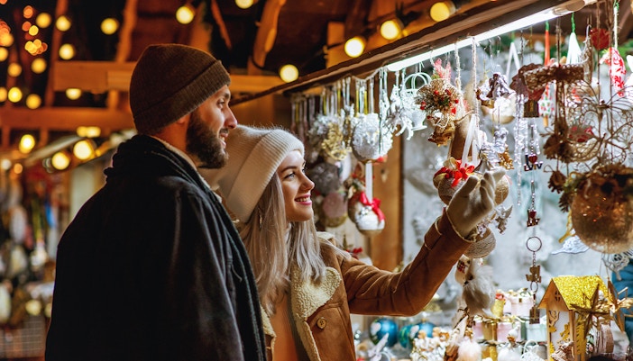 Couple purchasing decorations at a Christmas market in a festive setting.