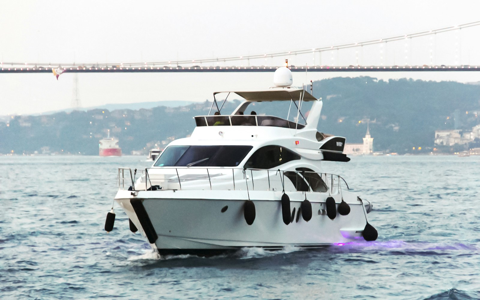 Luxury yacht cruising on the Bosphorus with a bridge in the background.