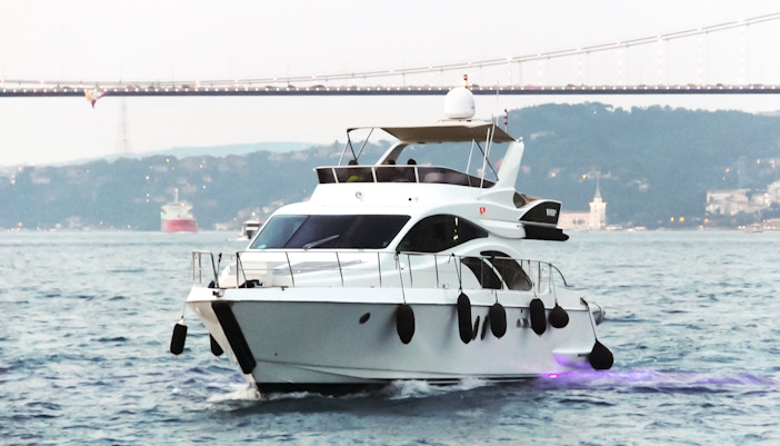 Luxury yacht cruising on the Bosphorus with a bridge in the background.
