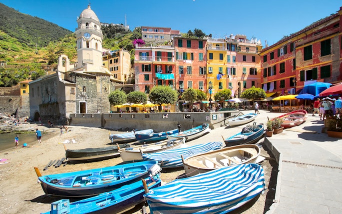 Boats docked near colorful buildings and a church tower in Vernazza, Italy.