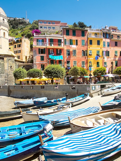 Boats docked near colorful buildings and a church tower in Vernazza, Italy.