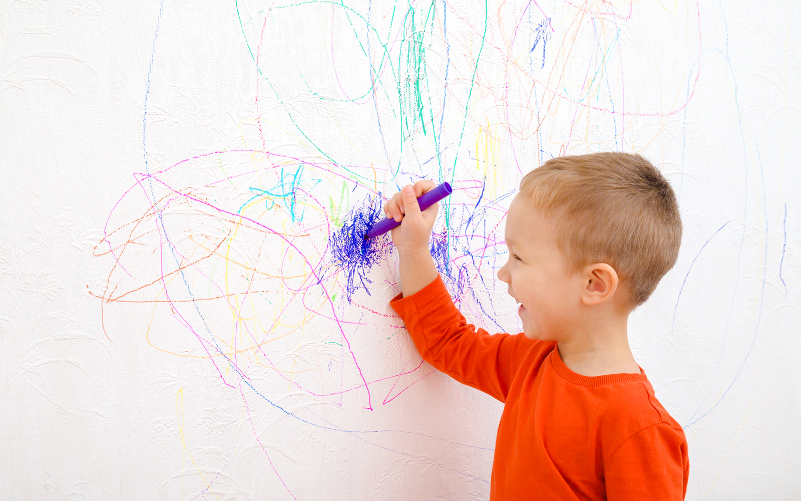 Boy drawing colorful doodles on a white wall.
