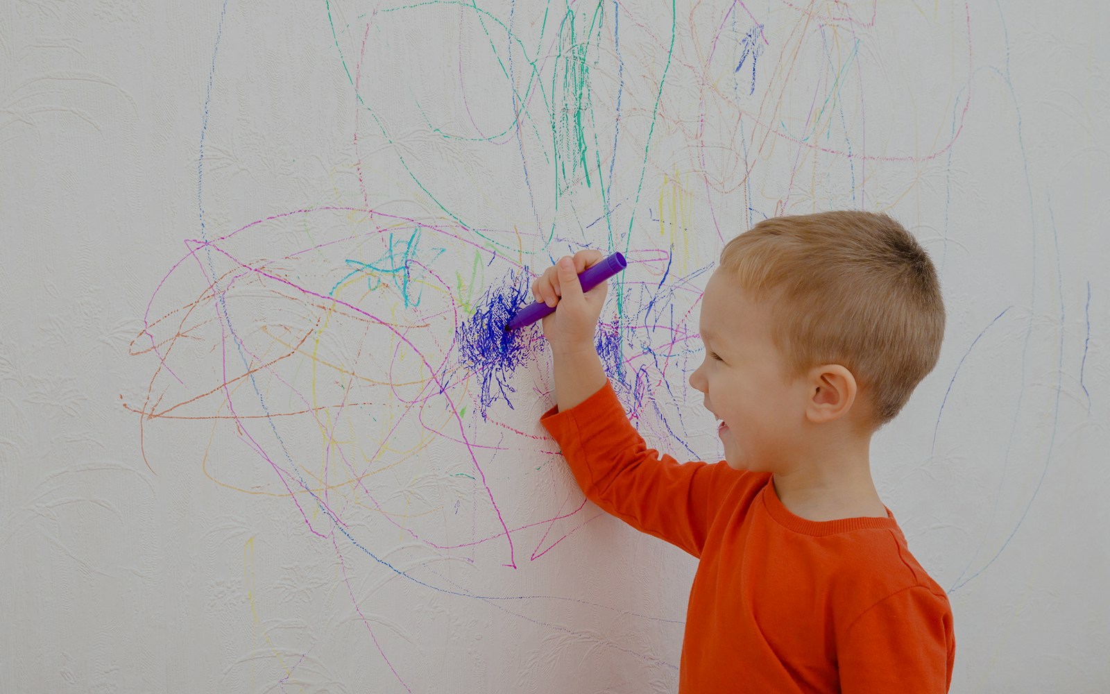 Boy drawing colorful doodles on a white wall.