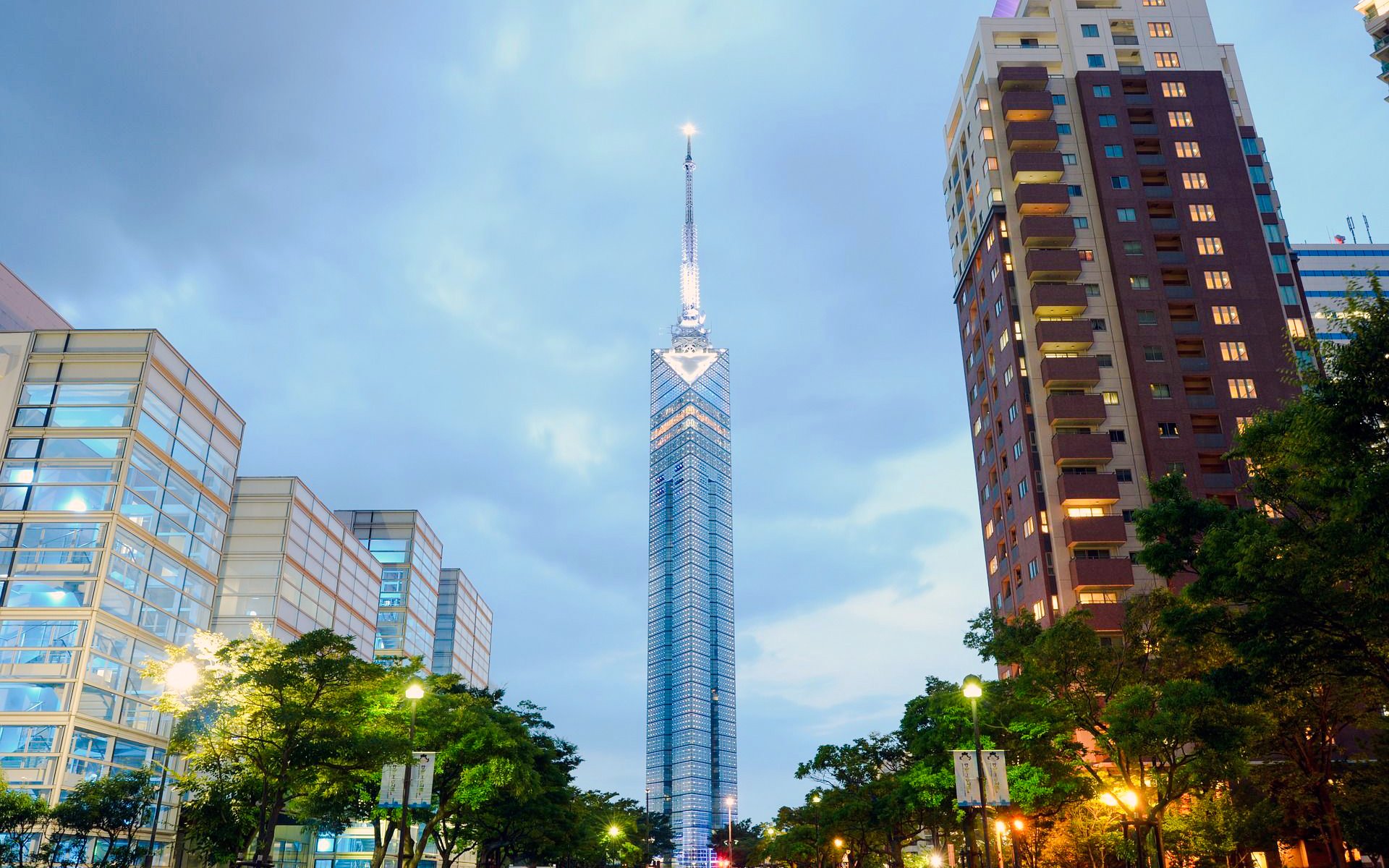 Fukuoka Tower illuminated at dusk in Fukuoka City, surrounded by modern buildings.