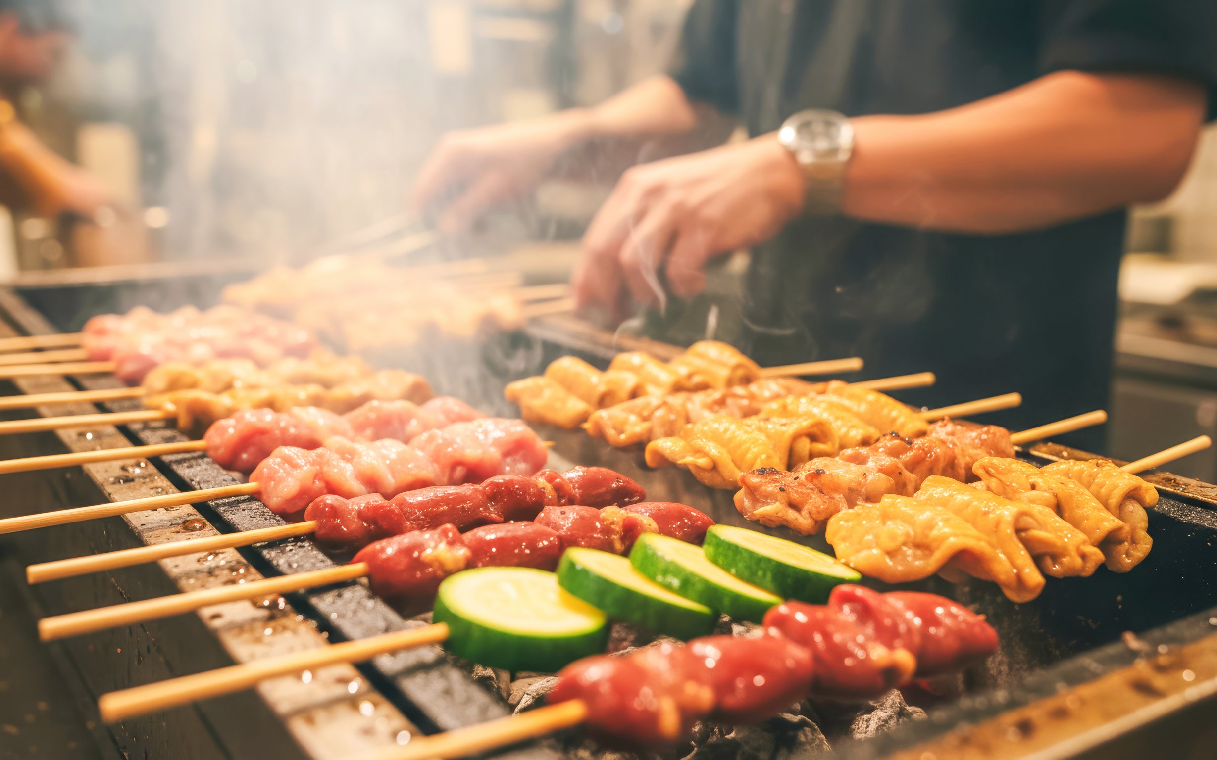 Yakitori skewers grilling with zucchini slices on a barbecue.