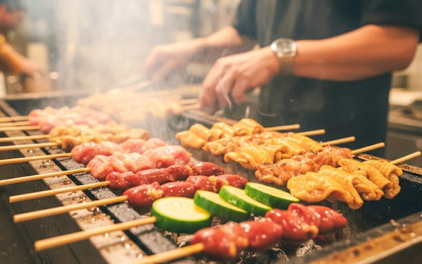 Yakitori skewers grilling with zucchini slices on a barbecue.
