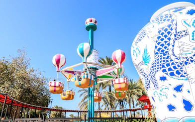 Colorful balloon ride at Al Montazah Parks, Island of Legends, with palm trees and decorative vase.