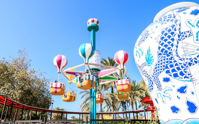 Colorful balloon ride at Al Montazah Parks, Island of Legends, with palm trees and decorative vase.