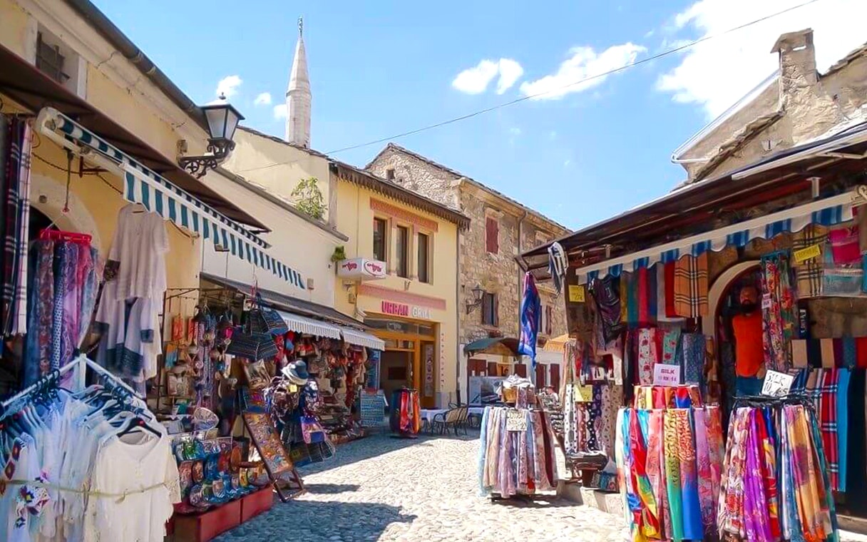 Old town market in Mostar with colorful textiles and stone buildings.