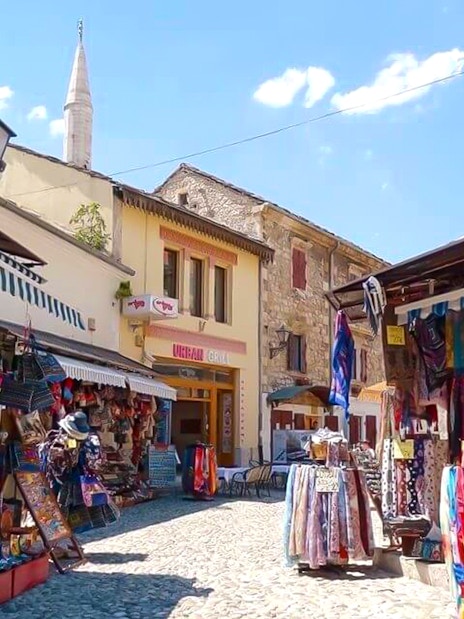 Old town market in Mostar with colorful textiles and stone buildings.