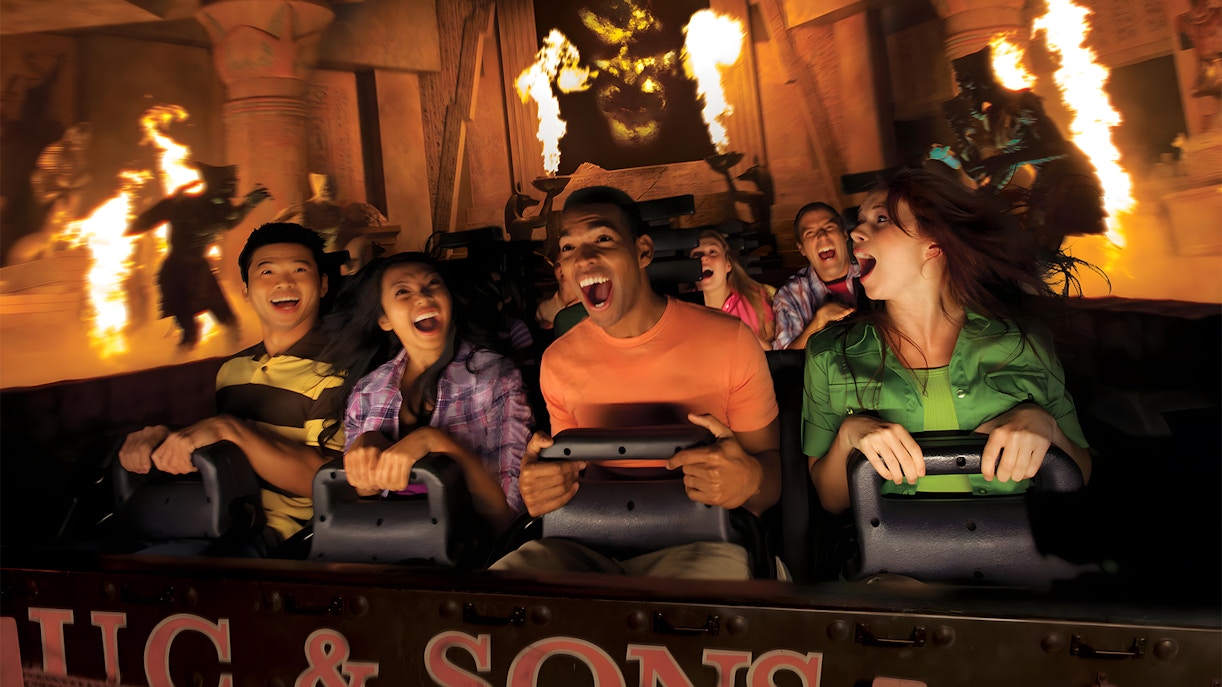 Visitors on a thrilling ride at Universal Studios Hollywood with fire effects in the background.