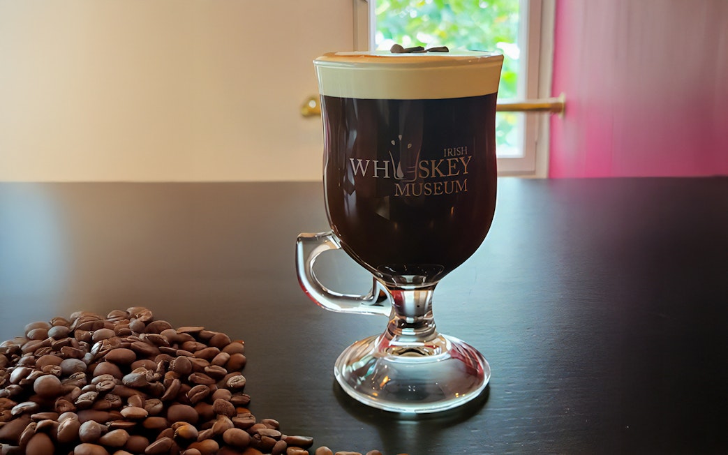 Irish coffee with cream at the Irish Whiskey Museum, Dublin, beside coffee beans.
