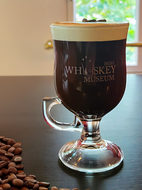 Irish coffee with cream at the Irish Whiskey Museum, Dublin, beside coffee beans.