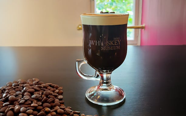 Irish coffee with cream at the Irish Whiskey Museum, Dublin, beside coffee beans.