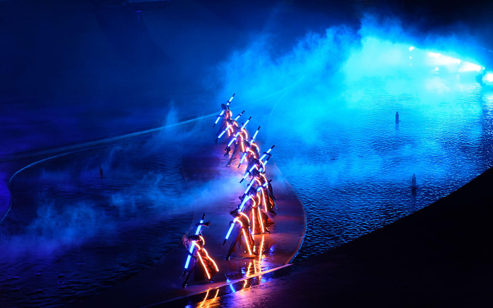 Performers with illuminated costumes in a blue-lit water stage at Kiss of the Sea Show.
