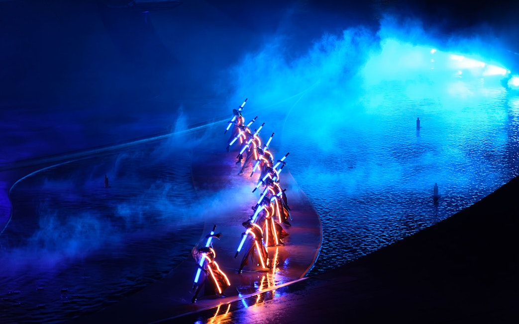 Performers with illuminated costumes in a blue-lit water stage at Kiss of the Sea Show.