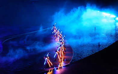 Performers with illuminated costumes in a blue-lit water stage at Kiss of the Sea Show.