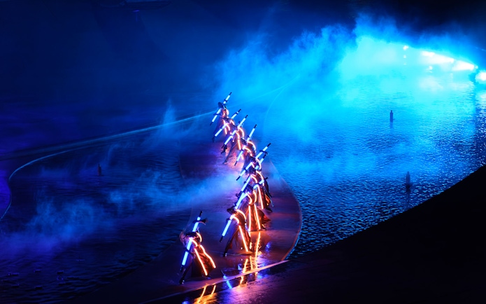 Performers with illuminated costumes in a blue-lit water stage at Kiss of the Sea Show.