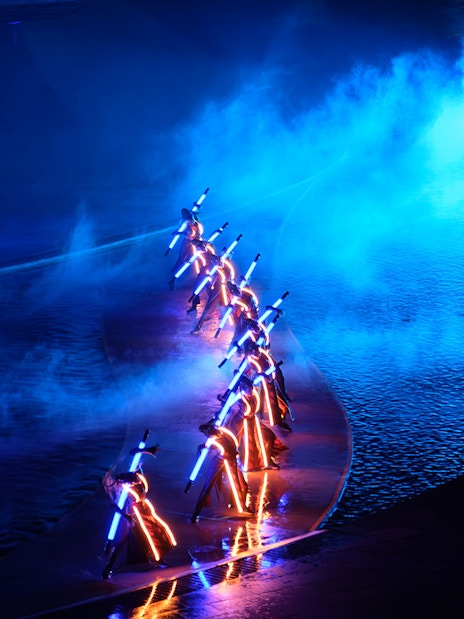 Performers with illuminated costumes in a blue-lit water stage at Kiss of the Sea Show.