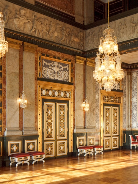 Interior of a grand hall in Copenhagen with ornate chandeliers and decorative walls.