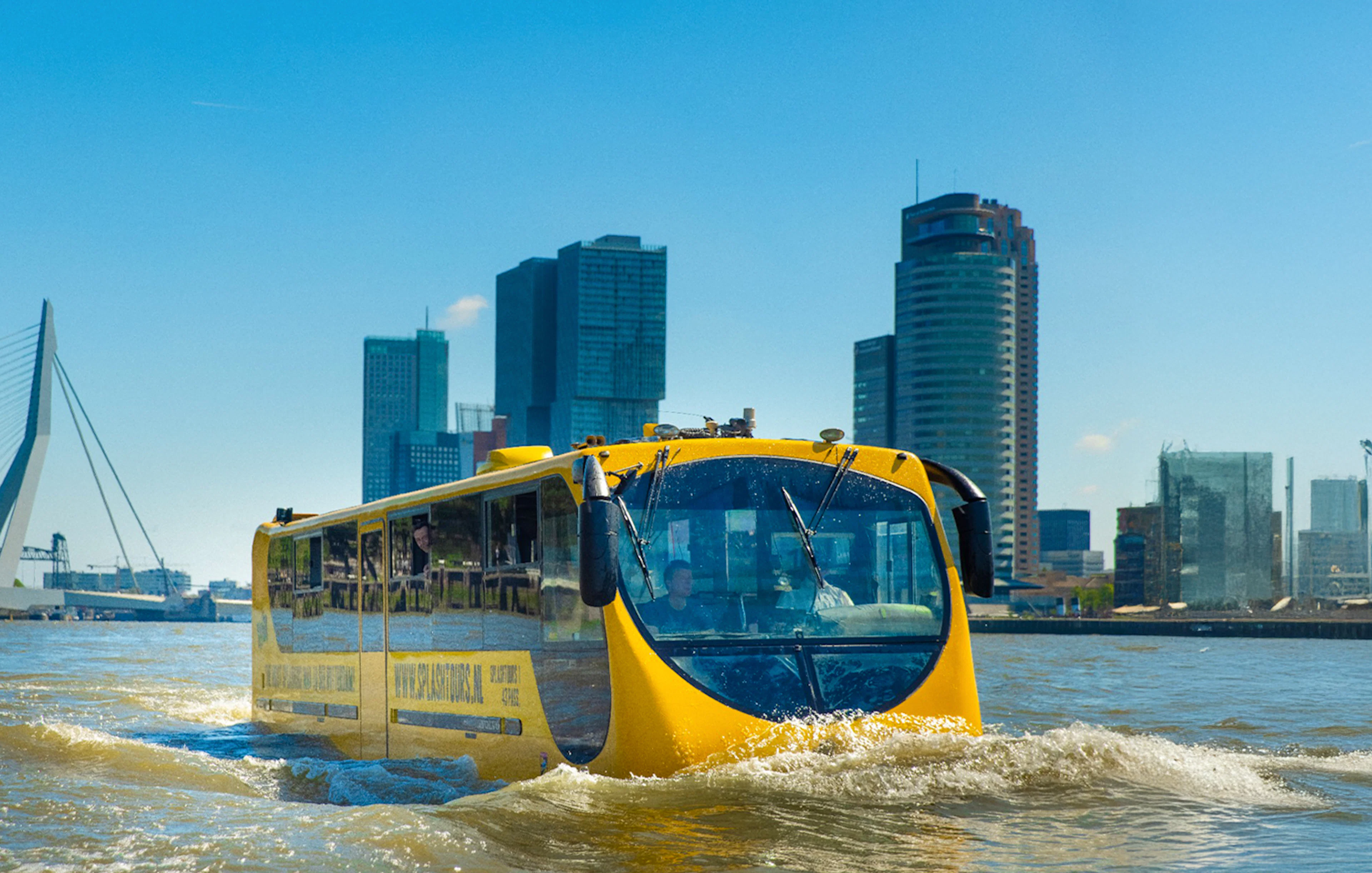 Amphibious bus on Rotterdam waterway with city skyline in background.