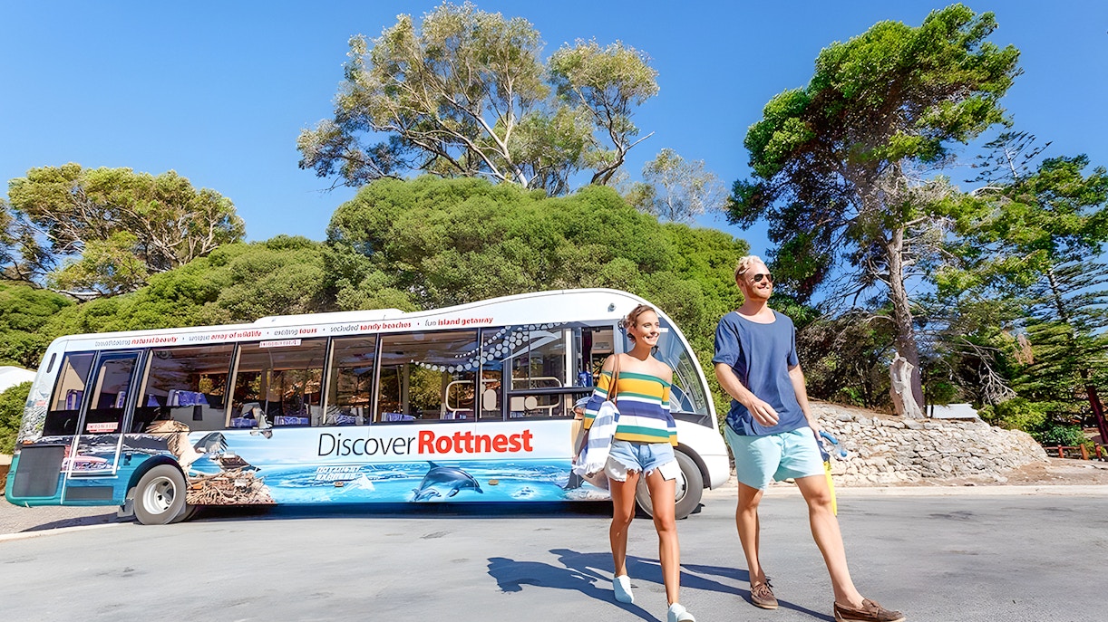 Group of tourists enjoying the Rottnest Island Guided Bus Tour with a return ferry from Perth or Fremantle, with a scenic view of the island's coastline in the background
