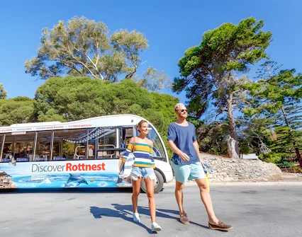 Tourists walking near a bus on Rottnest Island with coastal scenery in the background.
