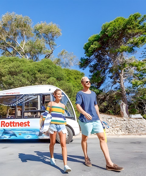 Tourists walking near a bus on Rottnest Island with coastal scenery in the background.