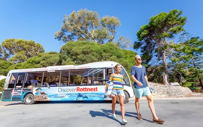 Tourists walking near a bus on Rottnest Island with coastal scenery in the background.