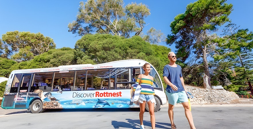 Tourists walking near a bus on Rottnest Island with coastal scenery in the background.