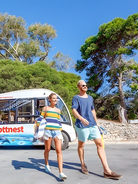 Tourists walking near a bus on Rottnest Island with coastal scenery in the background.