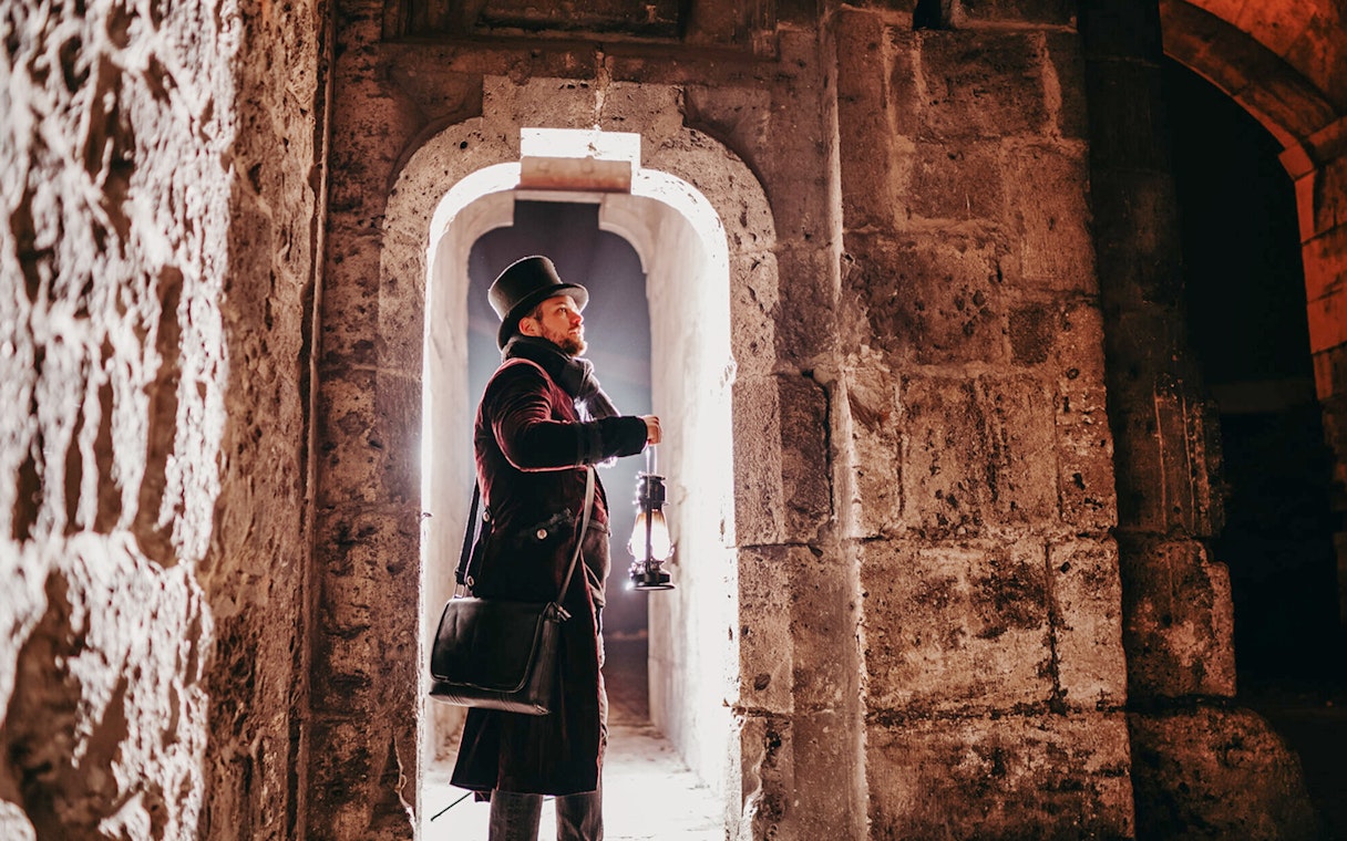 Man in period costume holding lantern in Buda Castle passageway, Budapest evening tour.