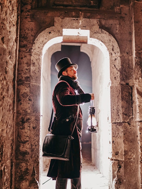 Man in period costume holding lantern in Buda Castle passageway, Budapest evening tour.