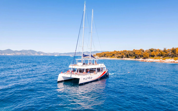 Catamaran sailing near Lérins Island, Marina Bay of Angels, with coastline view.