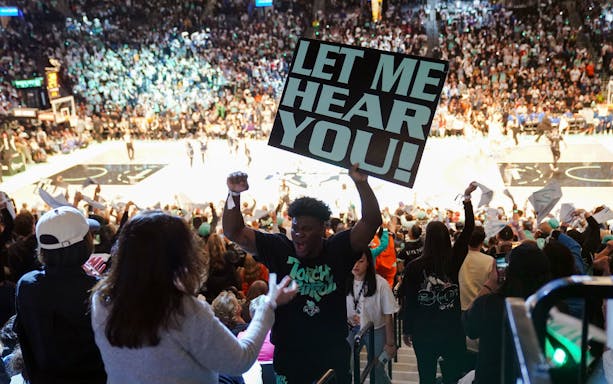 Fans cheering at New York Liberty basketball game with a "Let Me Hear You" sign.