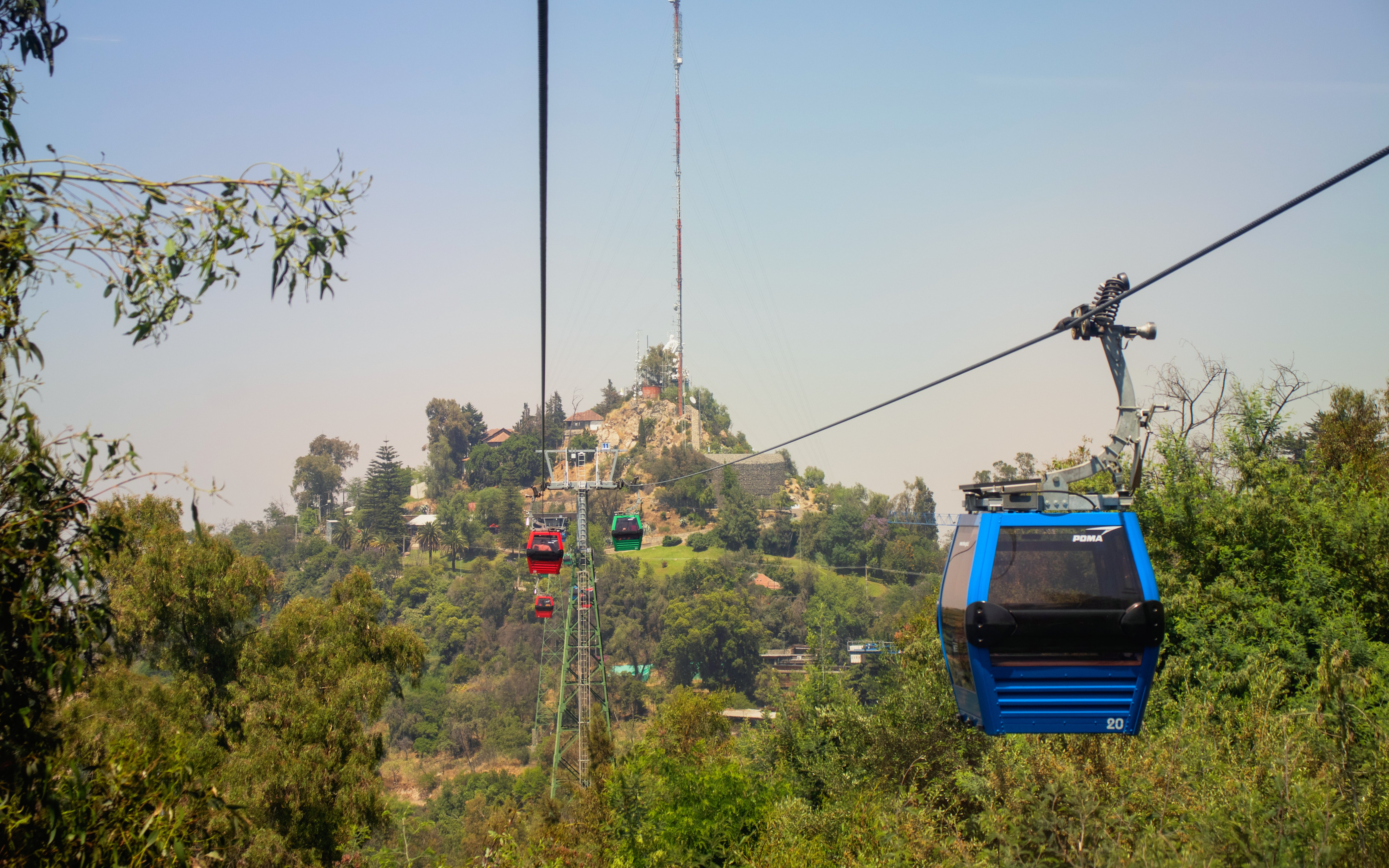 Cable car ascending Cerro San Cristobal in Santiago, Chile, with hill and blue sky in background.