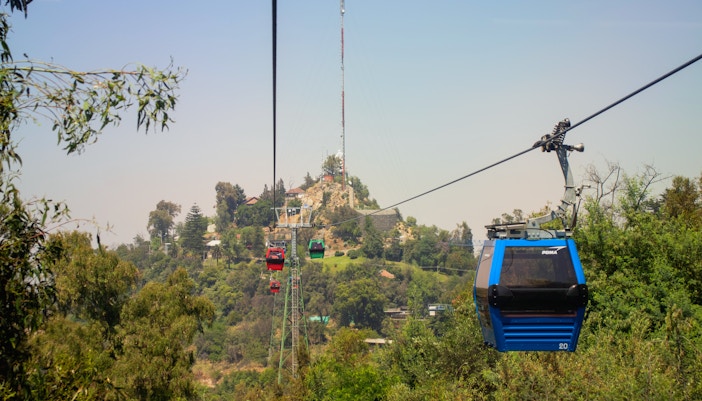 Cable car ascending Cerro San Cristobal in Santiago, Chile, with hill and blue sky in background.