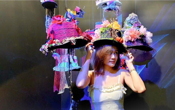 Visitor trying on whimsical hats at Alice Saves Wonderland: The Immersive Journey exhibit.
